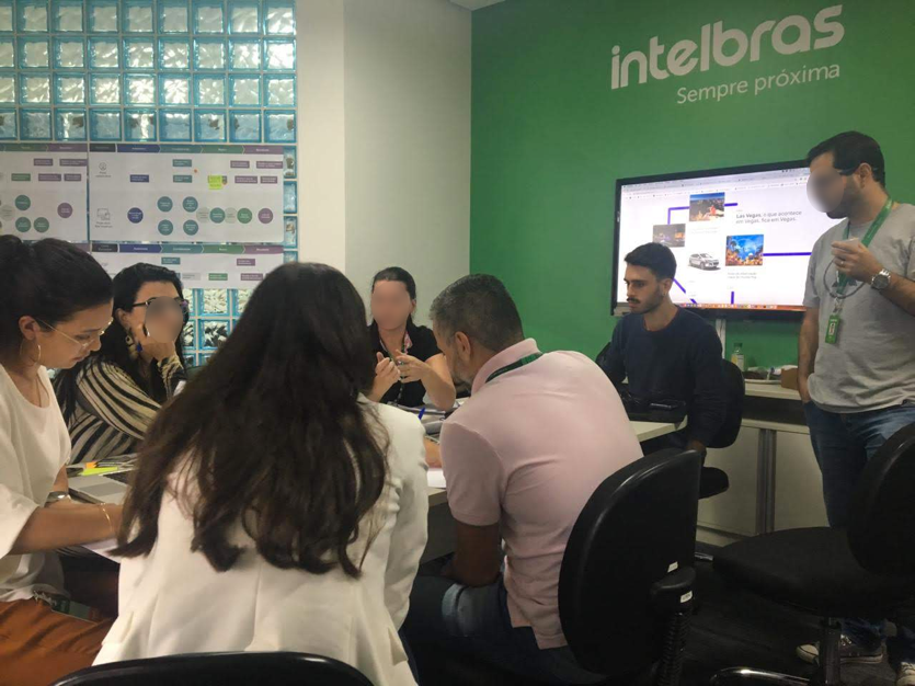 Workshop discussion around a table, with a slide on an Intelbras-branded screen guiding the session